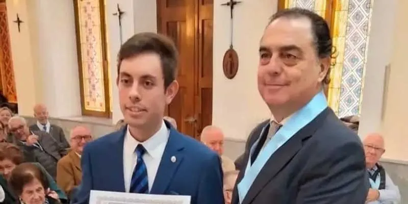 Eduardo Aranda Hortelano, con traje azul, sostiene el diploma junto a un miembro de la asociación con banda celeste, en la capilla del colegio.